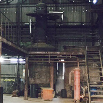 The thin-film evaporator column rising through the plant floor, with a red vessel beside it